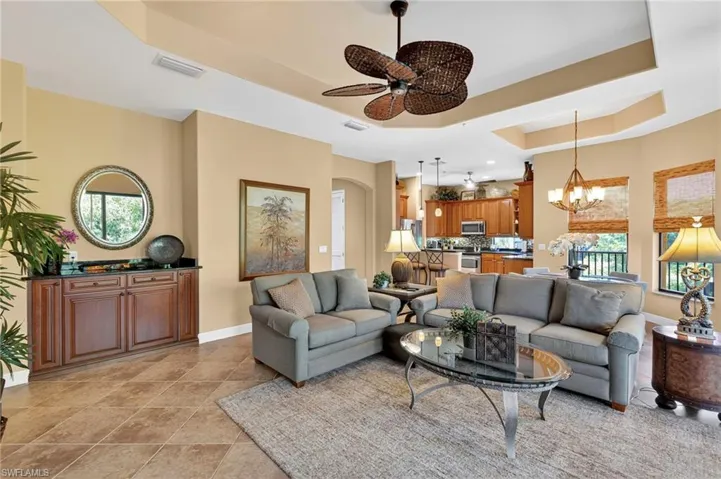 Living area with a raised ceiling, a chandelier, ceiling fan, and light tile patterned floors