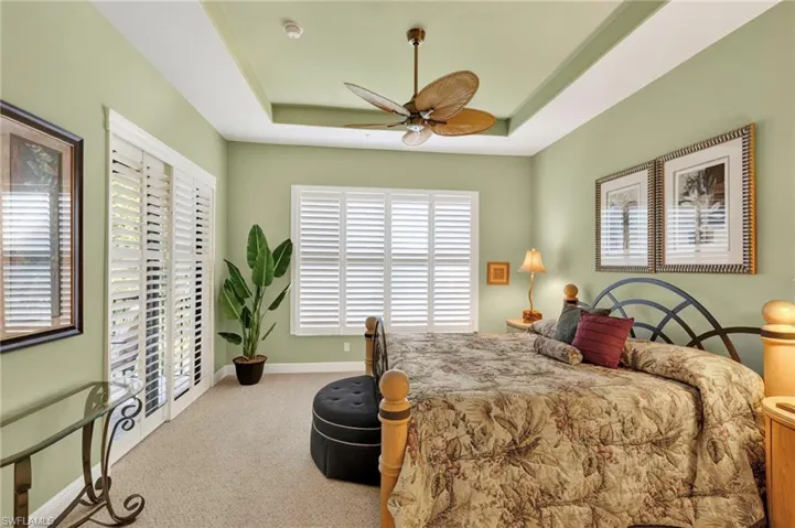 Bedroom featuring a raised ceiling, light carpet, and ceiling fan