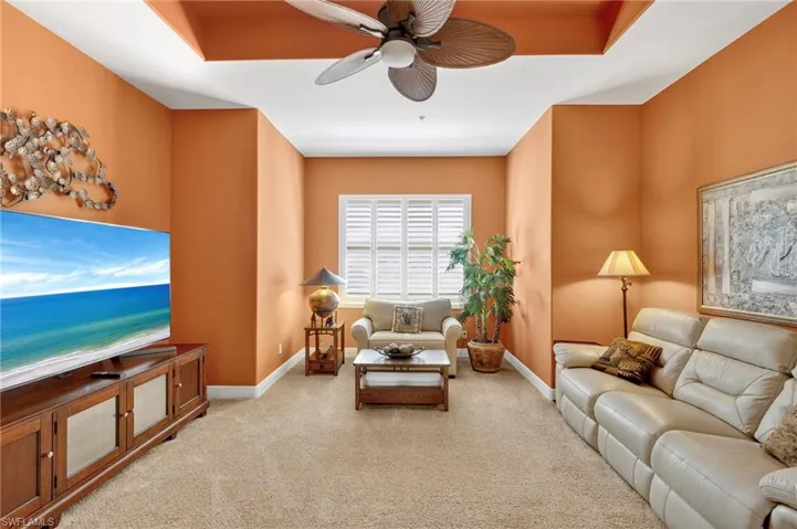 Living area with light colored carpet, a ceiling fan, and a raised ceiling