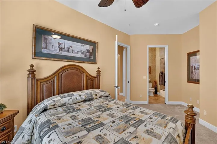 Bedroom featuring a ceiling fan, light colored carpet, and ensuite bath