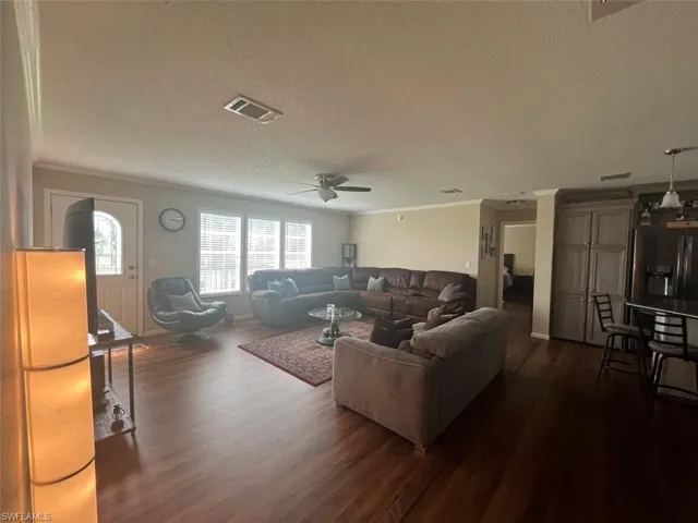 Living room featuring dark wood-type flooring, a textured ceiling, ceiling fan, and crown molding