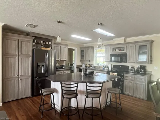 Kitchen featuring black appliances, ornamental molding, dark hardwood / wood-style floors, a kitchen island, and decorative light fixtures