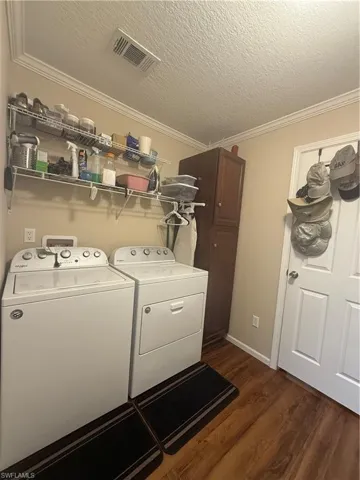 Laundry area featuring a textured ceiling, separate washer and dryer, dark wood-type flooring, and ornamental molding