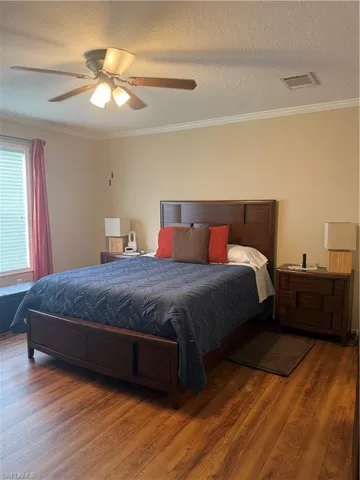 Bedroom with ceiling fan, dark hardwood / wood-style floors, ornamental molding, and a textured ceiling