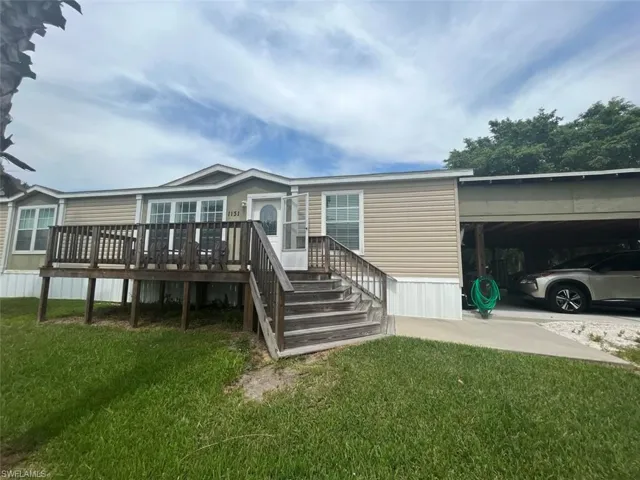Back of house featuring a wooden deck, a lawn, and a carport