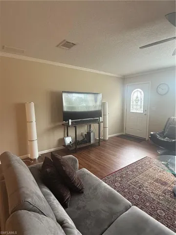 Living room featuring wood-type flooring, a textured ceiling, ceiling fan, and crown molding