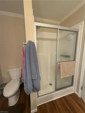 Bathroom with wood-type flooring, toilet, walk in shower, and crown molding
