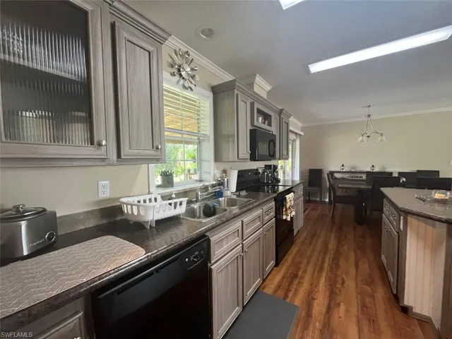 Kitchen with black appliances, crown molding, dark hardwood / wood-style floors, sink, and a chandelier
