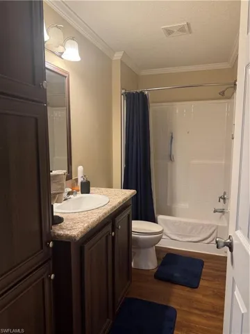 Bathroom featuring crown molding, a textured ceiling, toilet, vanity, and hardwood / wood-style flooring