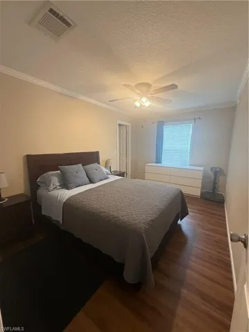 Bedroom featuring a textured ceiling, ceiling fan, dark hardwood / wood-style floors, and crown molding