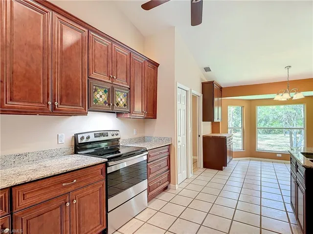 Kitchen with electric stove, lofted ceiling, light tile flooring, and ceiling fan with notable chandelier