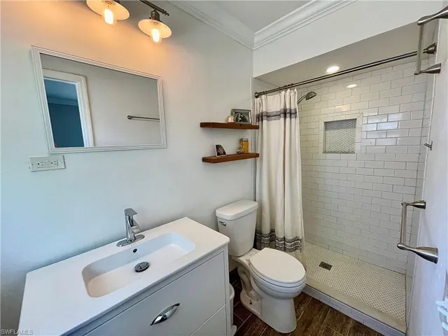 Bathroom with curtained shower, toilet, vanity, wood-type flooring, and ornamental molding
