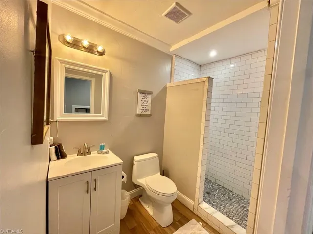 Bathroom with vanity, toilet, a tile shower, and wood-type flooring