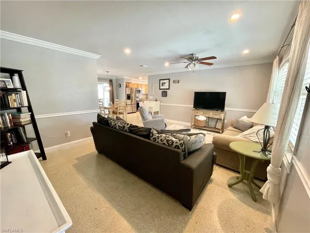 Living room featuring light carpet, ornamental molding, and ceiling fan