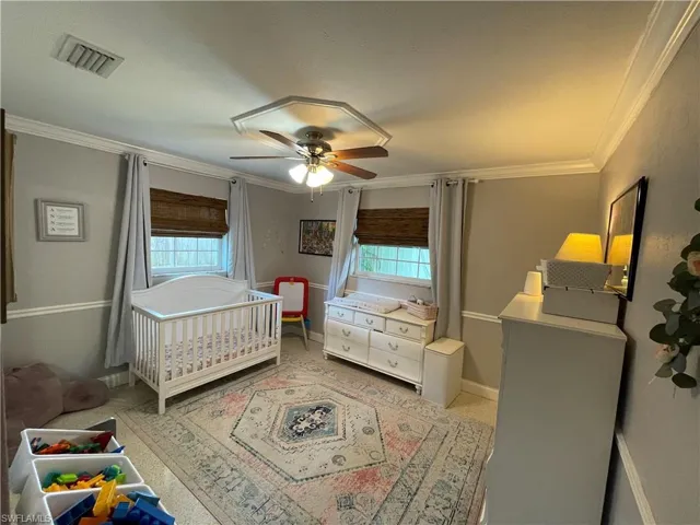 Carpeted bedroom featuring ornamental molding, multiple windows, a crib, and ceiling fan