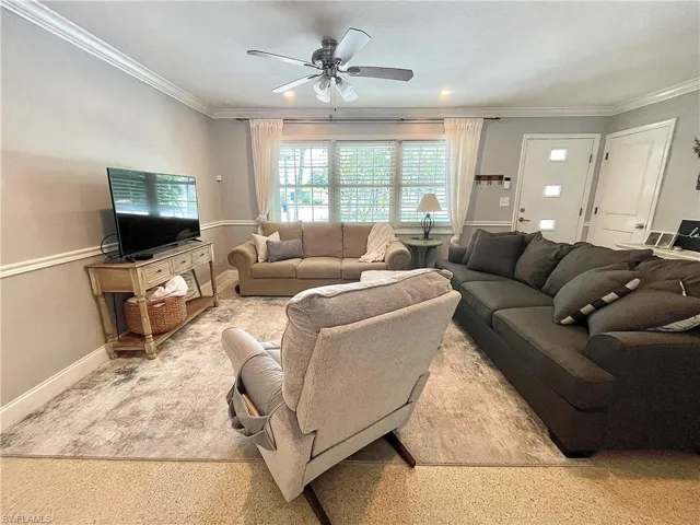 Carpeted living room with ornamental molding and ceiling fan