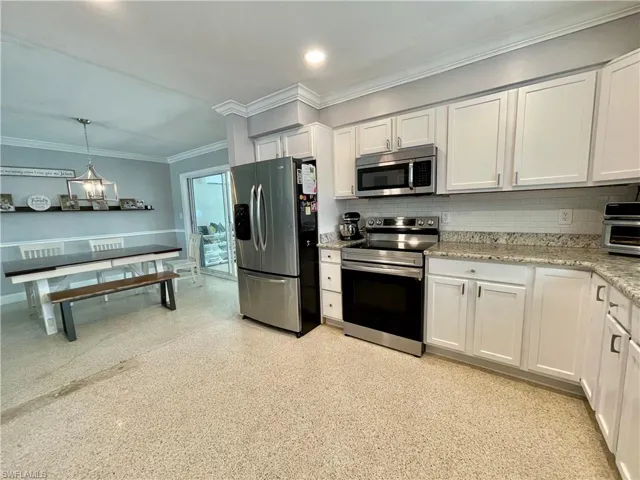 Kitchen featuring white cabinets, stainless steel appliances, hanging light fixtures, and ornamental molding