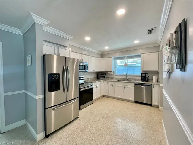 Kitchen featuring white cabinets, backsplash, appliances with stainless steel finishes, sink, and ornamental molding