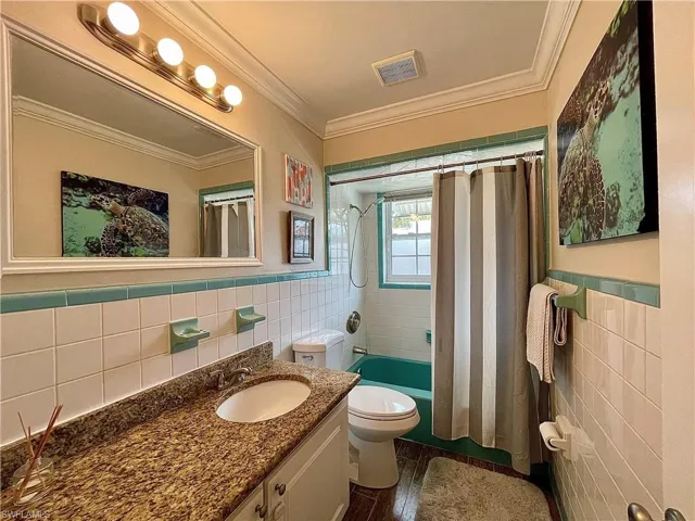 Full bathroom featuring vanity, shower / bathtub combination with curtain, tile walls, ornamental molding, and toilet