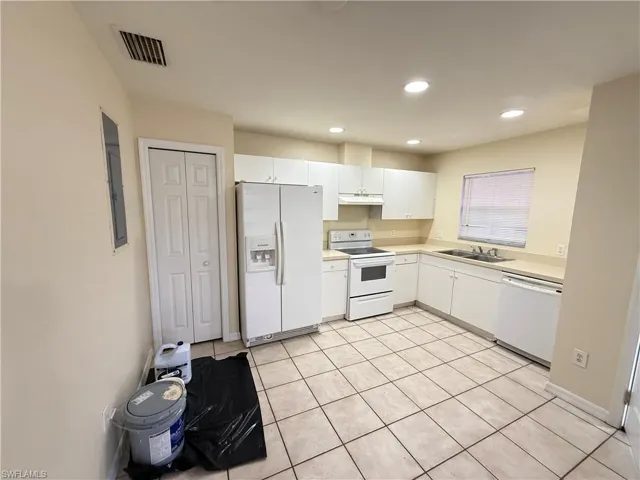 Kitchen with white appliances, white cabinets, light countertops, light tile patterned floors, and recessed lighting