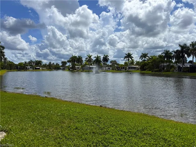 Expansive waterfront property featuring a manicured lawn, mature palm trees, and a decorative water fountain