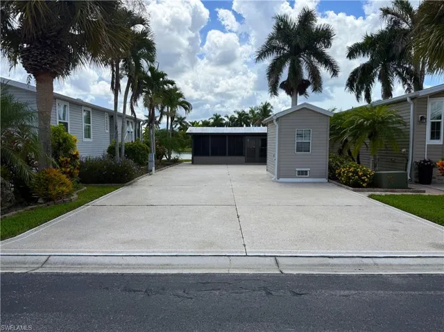 Expansive concrete driveway with landscaped borders, a utility shed, and an attached screened enclosure