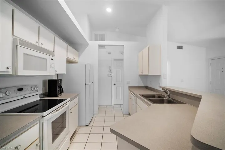 Kitchen featuring vaulted ceiling, sink, white appliances, and light tile patterned floors