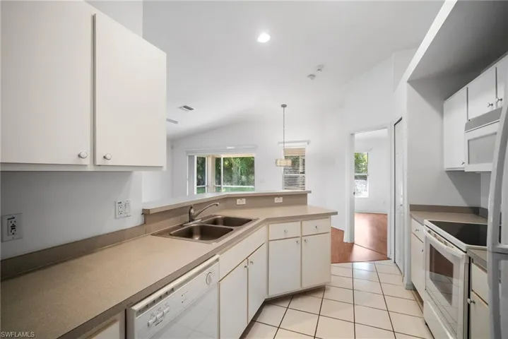 Kitchen with white appliances, sink, pendant lighting, light tile patterned floors, and lofted ceiling