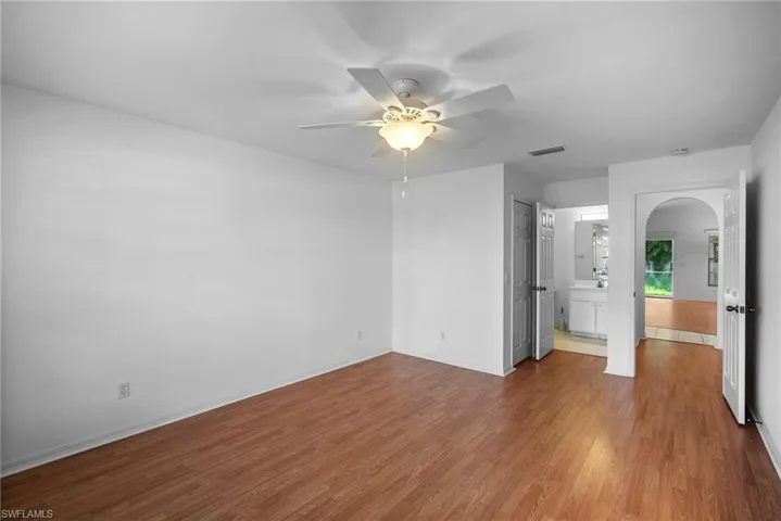 Unfurnished bedroom with ensuite bathroom, ceiling fan, and wood-type flooring