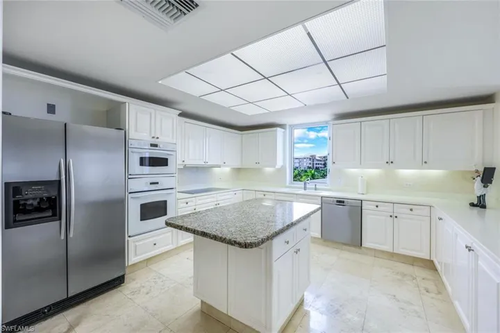 Kitchen with stainless steel appliances, white cabinets, sink, light tile patterned flooring, and a center island