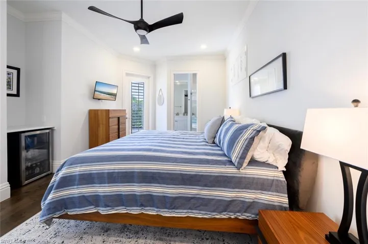 Bedroom featuring connected bathroom, ceiling fan, beverage cooler, ornamental molding, and dark wood-type flooring