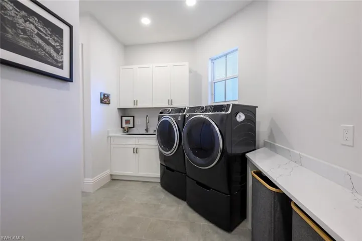 Laundry area with cabinets, separate washer and dryer, light tile patterned flooring, and sink