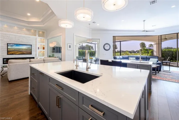 Kitchen with gray cabinets, a kitchen island with sink, light stone countertops, dark hardwood / wood-style flooring, and ceiling fan