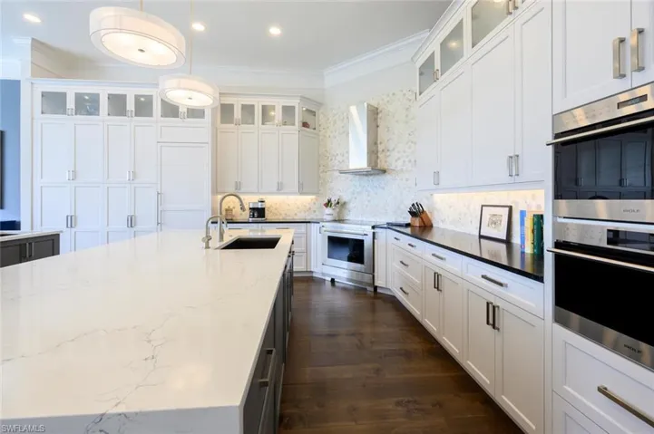 Kitchen with appliances with stainless steel finishes, hanging light fixtures, dark stone countertops, dark hardwood / wood-style flooring, and wall chimney exhaust hood