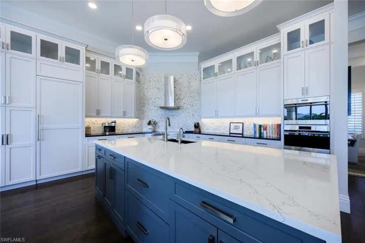 Kitchen with white cabinetry, stainless steel double oven, sink, and wall chimney range hood