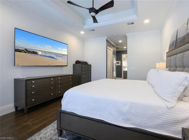 Bedroom featuring dark wood-type flooring, ceiling fan, a raised ceiling, and ornamental molding