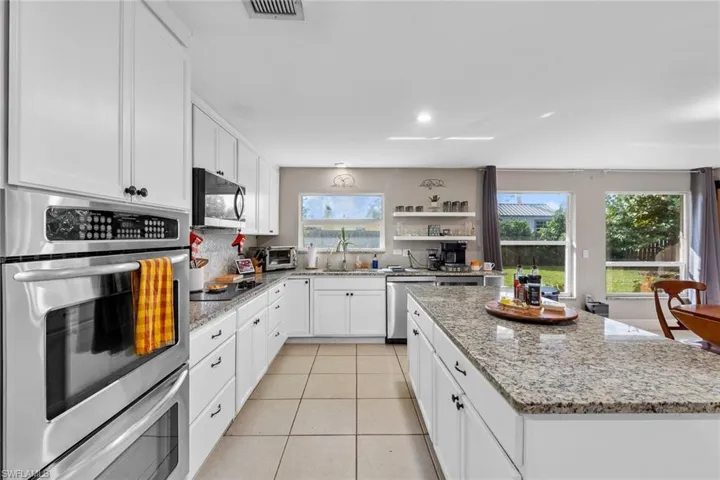 Kitchen with white cabinetry, light stone counters, plenty of natural light, a kitchen island, and appliances with stainless steel finishes