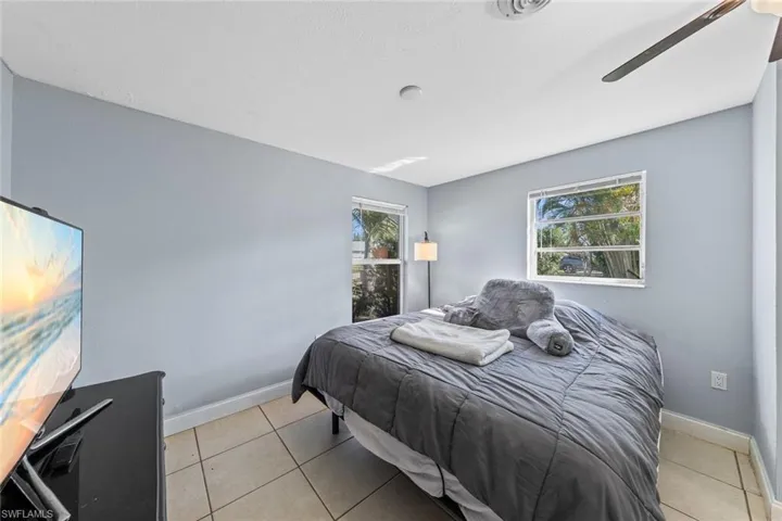 Tiled bedroom featuring multiple windows and ceiling fan