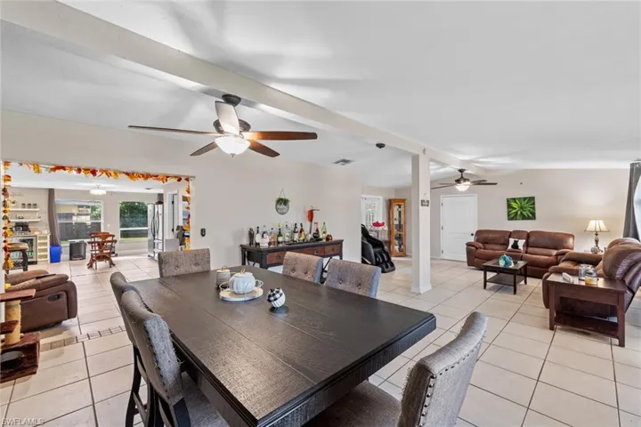 Tiled dining room with vaulted ceiling with beams, ceiling fan, and bar area