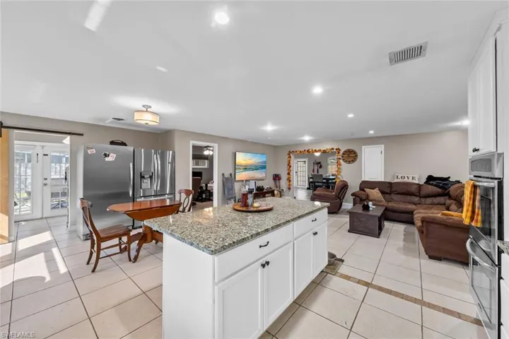 Kitchen with white cabinetry, light stone countertops, light tile patterned floors, a kitchen island, and appliances with stainless steel finishes