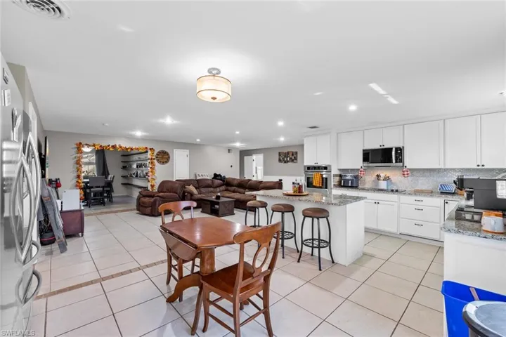 Kitchen featuring white cabinetry, light stone counters, a kitchen bar, light tile patterned flooring, and appliances with stainless steel finishes