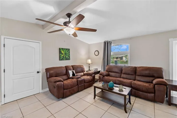 Tiled living room featuring ceiling fan and beamed ceiling