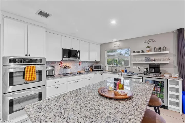 Kitchen featuring light stone counters, a breakfast bar, white cabinets, and appliances with stainless steel finishes