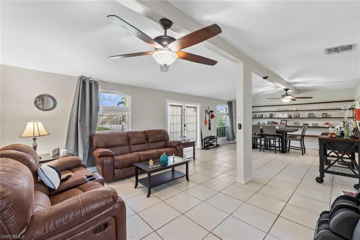 Living room with beamed ceiling, ceiling fan, light tile patterned flooring, and french doors