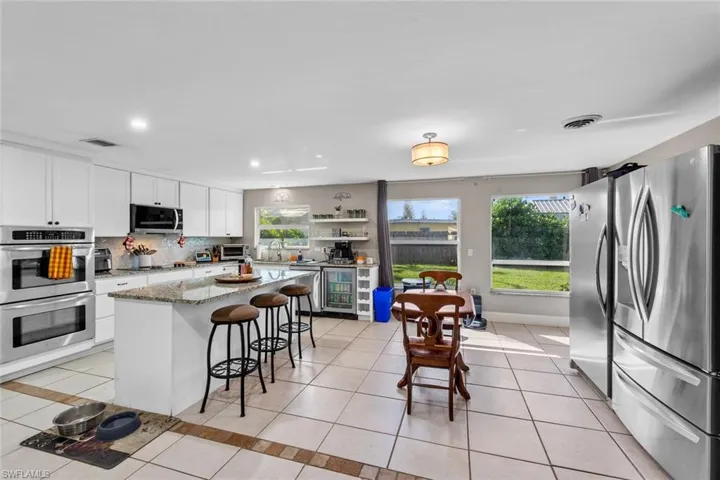 Kitchen featuring white cabinetry, stainless steel appliances, dark stone counters, a breakfast bar, and a kitchen island