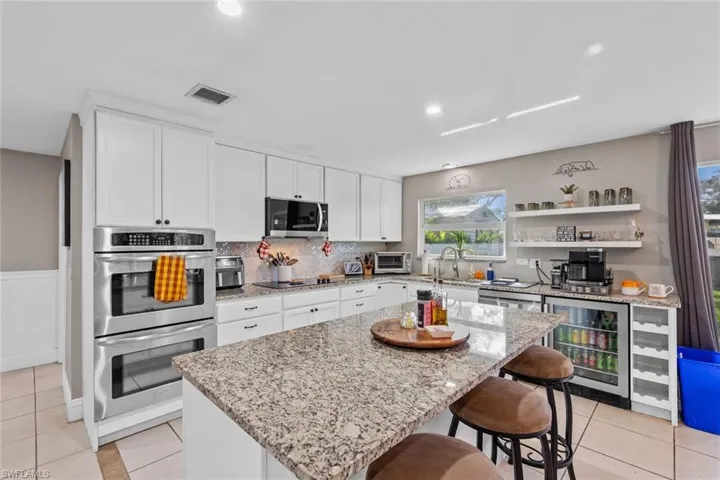 Kitchen featuring a center island, white cabinets, wine cooler, appliances with stainless steel finishes, and light stone counters