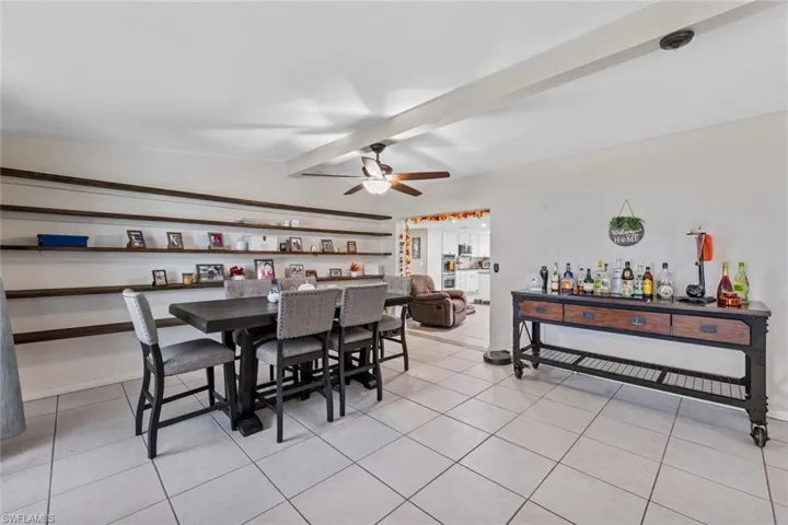 Tiled dining room with ceiling fan, lofted ceiling with beams, and indoor bar
