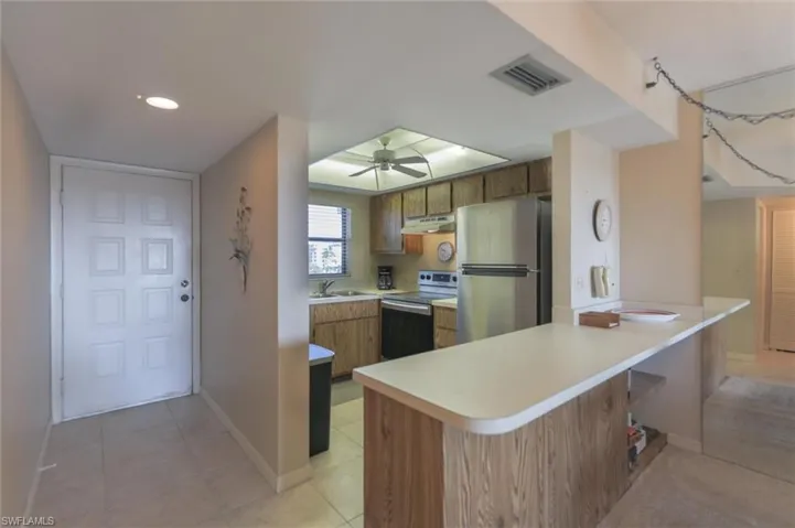Kitchen with kitchen peninsula, stainless steel appliances, ceiling fan, sink, and light tile floors