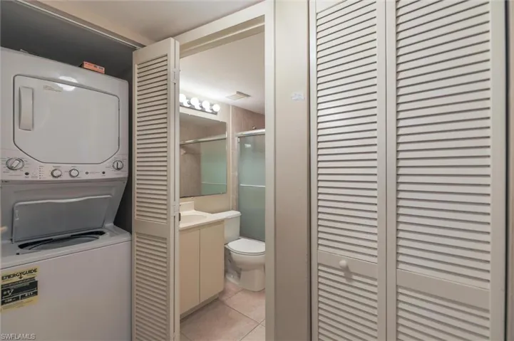 Bathroom with vanity with extensive cabinet space, stacked washer and dryer, toilet, and tile floors