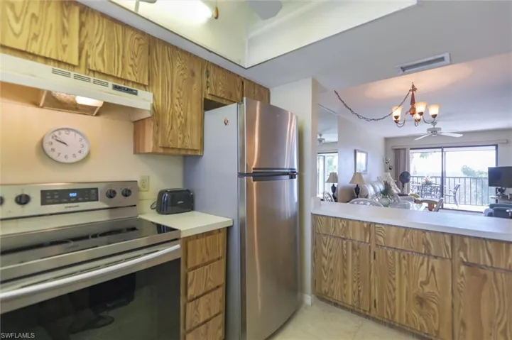 Kitchen with appliances with stainless steel finishes, pendant lighting, light tile flooring, and ceiling fan with notable chandelier